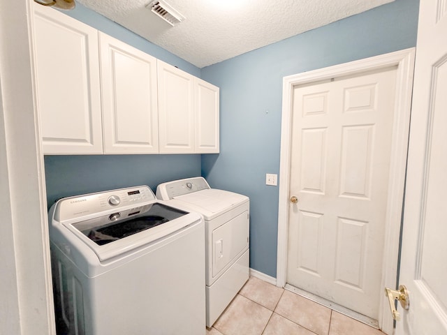 clothes washing area with cabinets, light tile patterned flooring, washing machine and dryer, and a textured ceiling