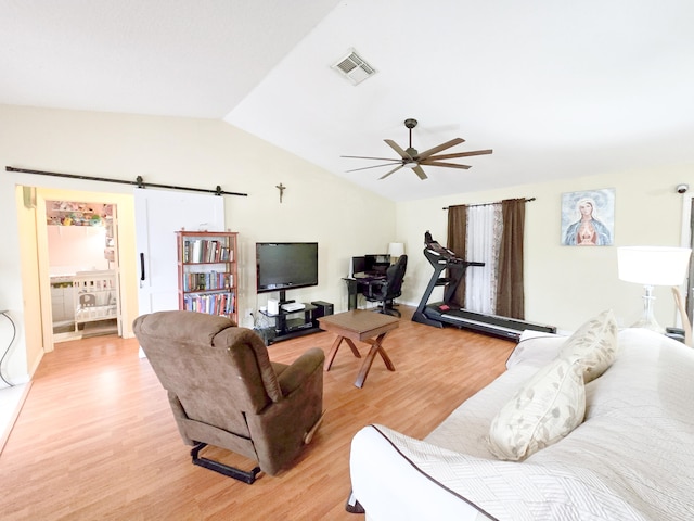 living room featuring vaulted ceiling, light hardwood / wood-style flooring, a barn door, and ceiling fan