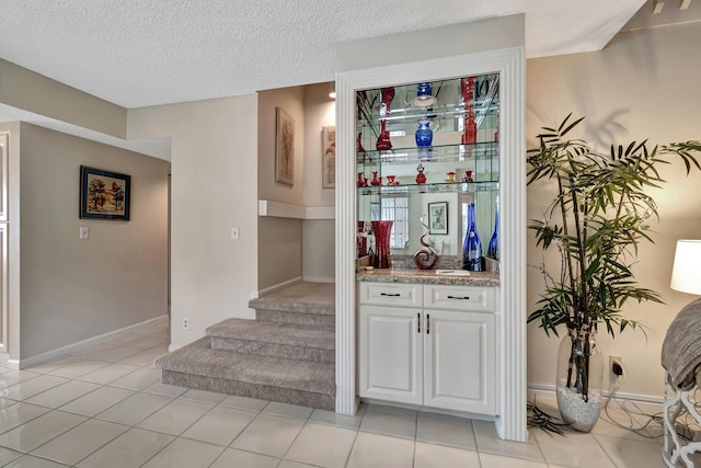 bar with light tile patterned floors, white cabinets, and a textured ceiling