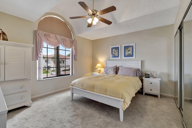 carpeted bedroom with a textured ceiling, lofted ceiling, a closet, and ceiling fan