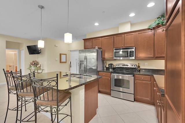 kitchen featuring decorative light fixtures, a breakfast bar, stainless steel appliances, sink, and dark stone countertops