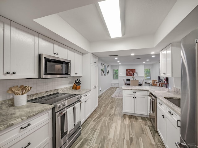 kitchen featuring kitchen peninsula, appliances with stainless steel finishes, light stone countertops, white cabinets, and light hardwood / wood-style floors