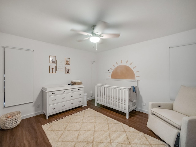 bedroom with ceiling fan, dark wood-type flooring, and a crib