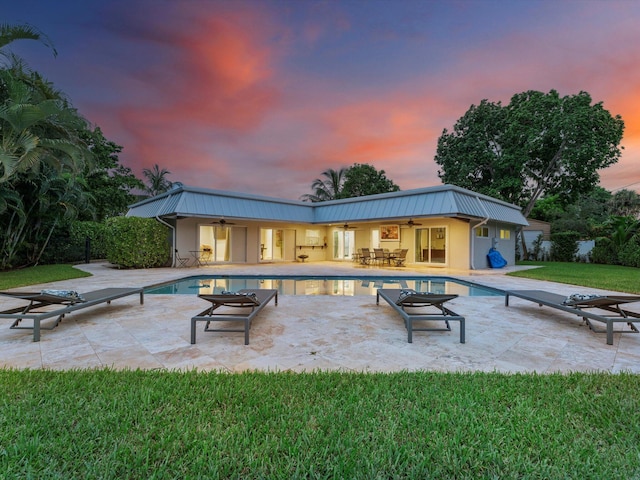 pool at dusk with a diving board, ceiling fan, and a patio area