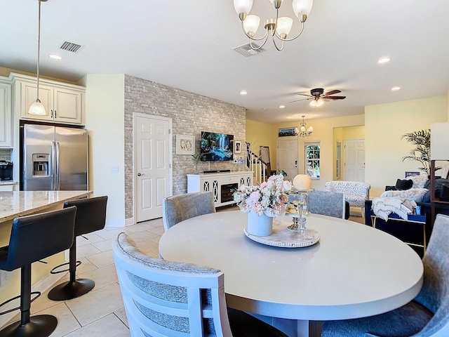 tiled dining space with ceiling fan with notable chandelier and a fireplace