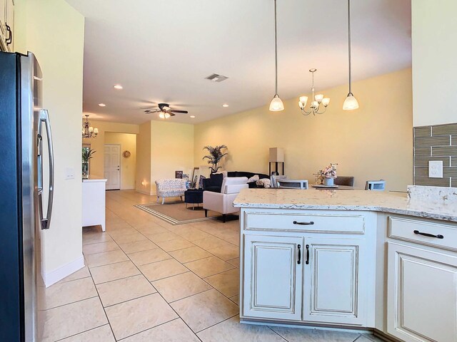 kitchen featuring decorative light fixtures, light stone counters, ceiling fan with notable chandelier, stainless steel fridge, and white cabinets