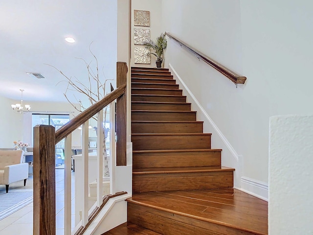 stairway with hardwood / wood-style floors and a notable chandelier