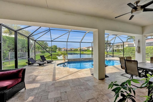 view of pool with glass enclosure, ceiling fan, a patio area, and a water view