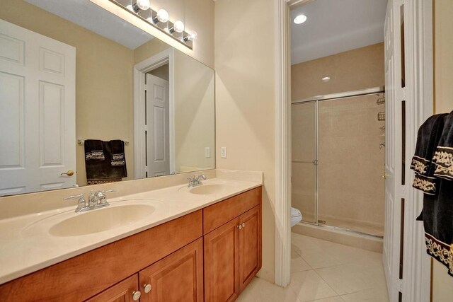 bathroom featuring a shower with shower door, tile patterned floors, double sink vanity, and toilet