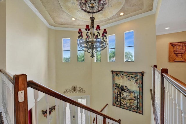 corridor with a raised ceiling, a chandelier, a healthy amount of sunlight, and ornamental molding