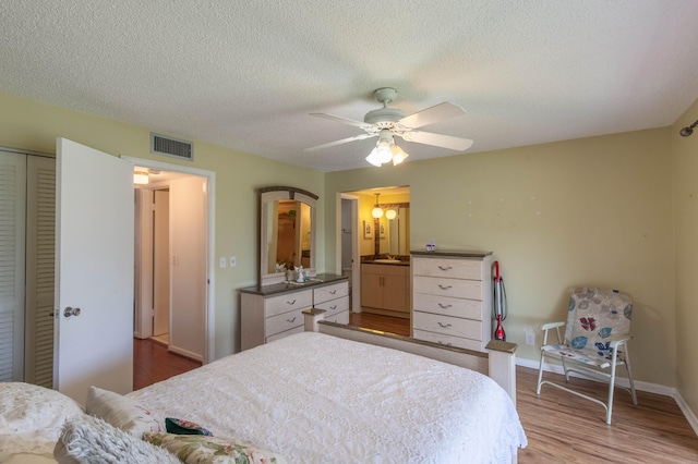 bedroom featuring a textured ceiling, hardwood / wood-style floors, ceiling fan, ensuite bath, and a closet