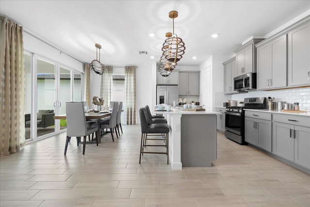 kitchen with appliances with stainless steel finishes, decorative light fixtures, gray cabinets, and an island with sink