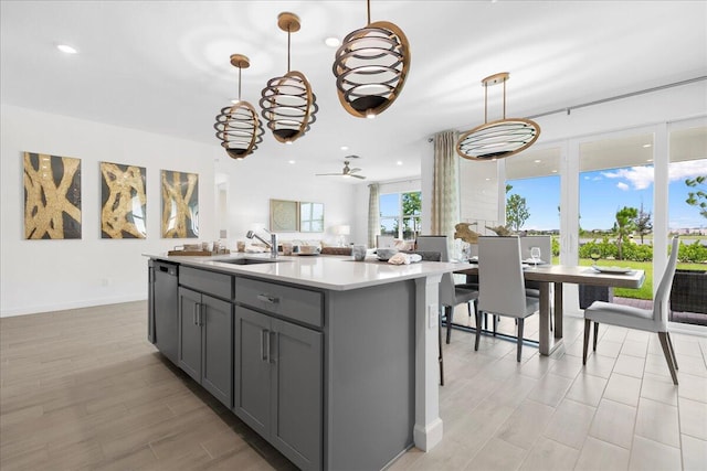 kitchen featuring ceiling fan, sink, hanging light fixtures, an island with sink, and gray cabinets