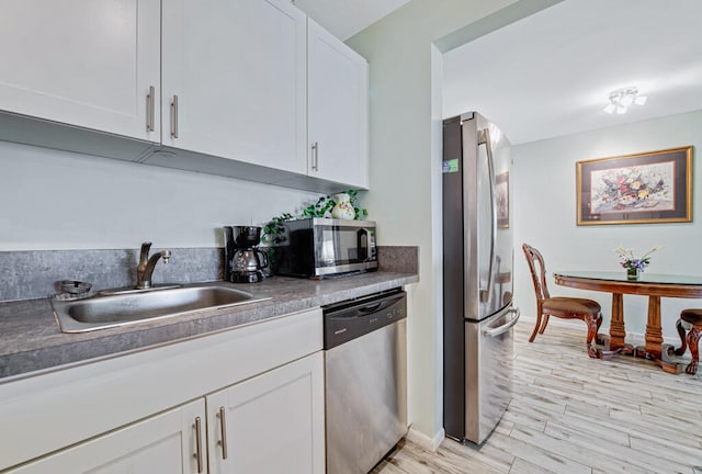 kitchen with light wood-type flooring, appliances with stainless steel finishes, white cabinetry, and sink