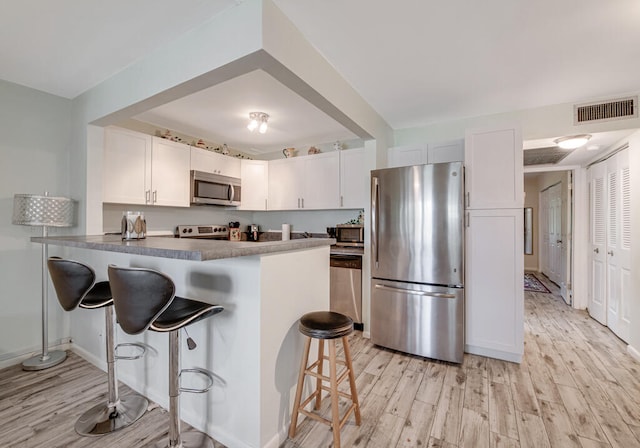 kitchen with a breakfast bar, kitchen peninsula, appliances with stainless steel finishes, and white cabinets