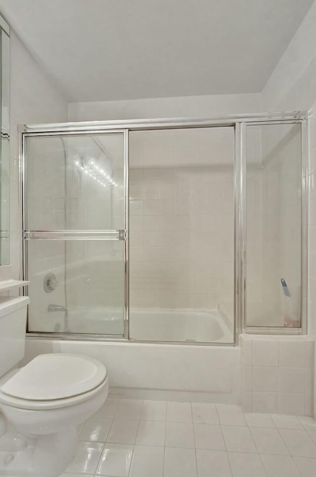 bathroom featuring tile patterned flooring, toilet, and shower / bath combination with glass door