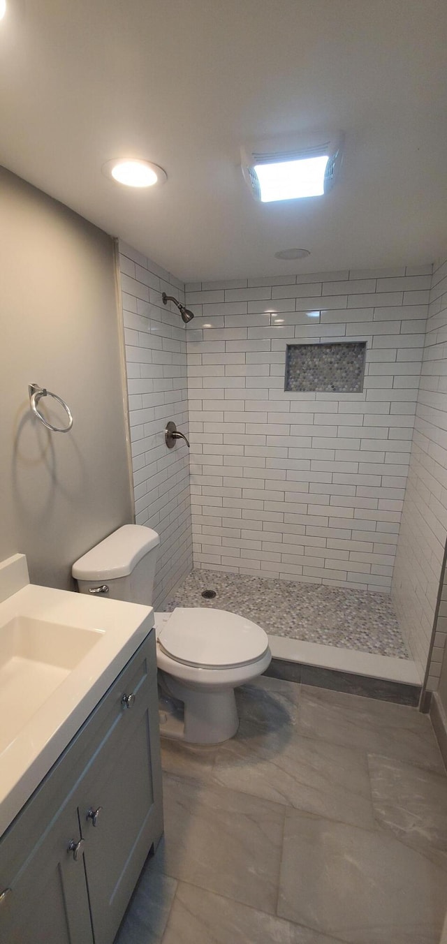 bathroom featuring tile patterned flooring, vanity, toilet, and tiled shower