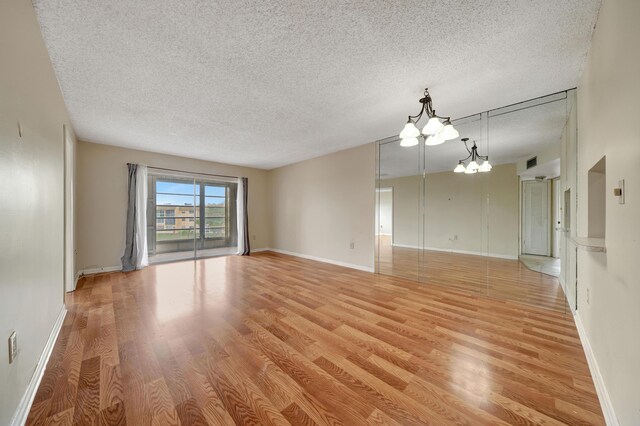 spare room with a textured ceiling, a chandelier, and light hardwood / wood-style floors