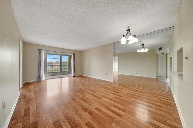 empty room with an inviting chandelier, light hardwood / wood-style flooring, and a textured ceiling