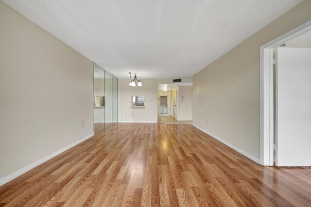 unfurnished living room with a notable chandelier, a textured ceiling, and light hardwood / wood-style floors