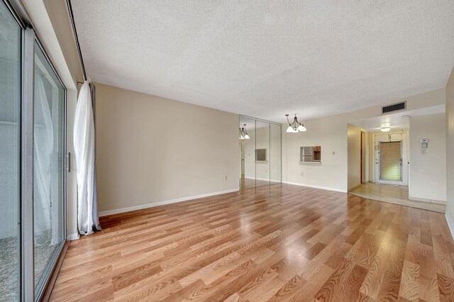 unfurnished room featuring a textured ceiling, a chandelier, and light hardwood / wood-style floors