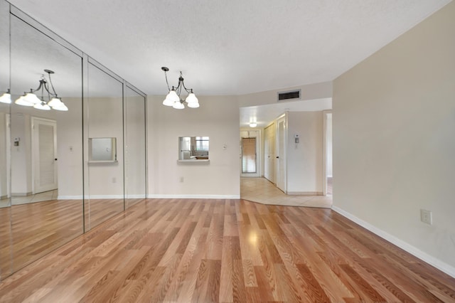 empty room featuring a textured ceiling, a chandelier, and light hardwood / wood-style flooring