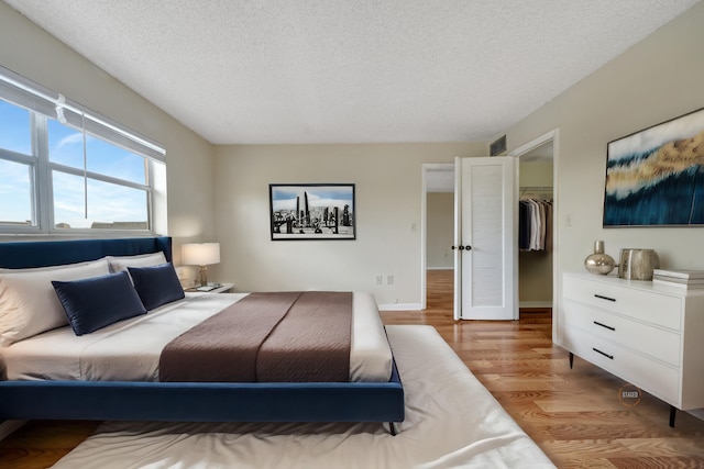 bedroom with a spacious closet, a closet, a textured ceiling, and light wood-type flooring