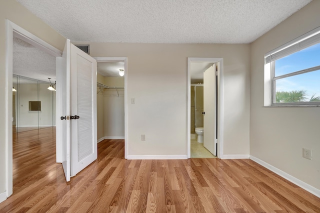 unfurnished bedroom featuring a spacious closet, a textured ceiling, light wood-type flooring, and a closet