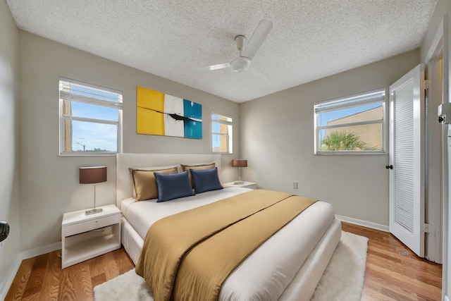 bedroom featuring ceiling fan, light wood-type flooring, a textured ceiling, and multiple windows