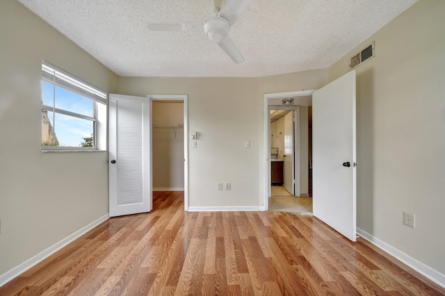 unfurnished bedroom featuring a textured ceiling, light tile patterned flooring, a walk in closet, a closet, and ceiling fan