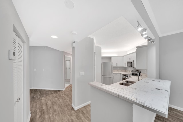 kitchen with light wood finished floors, baseboards, a peninsula, stainless steel appliances, and a sink