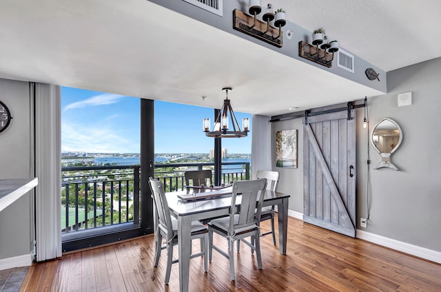 dining room featuring an inviting chandelier, a water view, a barn door, and hardwood / wood-style flooring