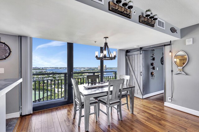 dining space featuring hardwood / wood-style floors, a barn door, a water view, and a chandelier