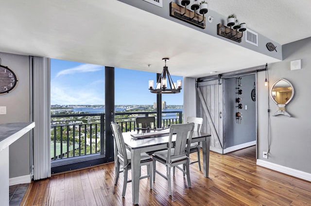 dining area with a chandelier, a water view, a barn door, and dark hardwood / wood-style flooring