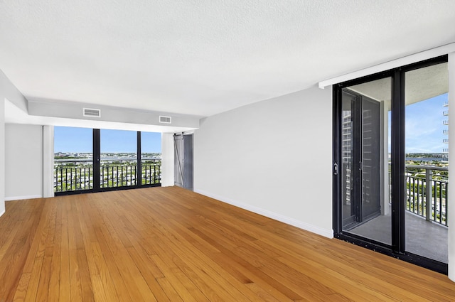 spare room with a wall of windows, wood-type flooring, a textured ceiling, and a wealth of natural light