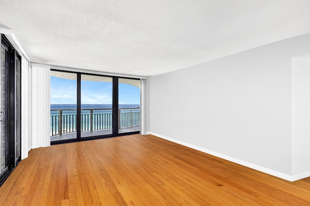 unfurnished room featuring light hardwood / wood-style flooring, expansive windows, a textured ceiling, and a water view