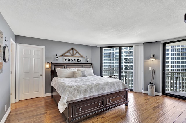 bedroom with multiple windows, access to exterior, wood-type flooring, and a textured ceiling