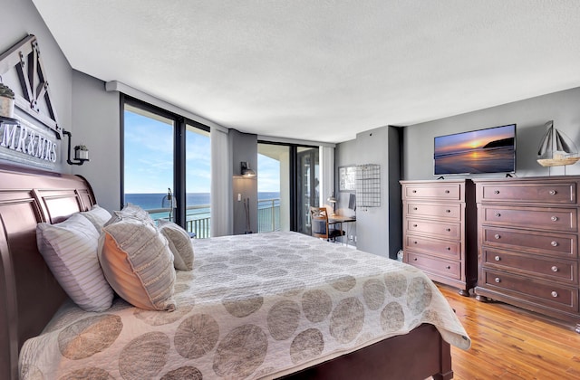 bedroom featuring floor to ceiling windows, light hardwood / wood-style flooring, access to outside, and a textured ceiling