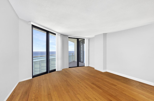 spare room featuring expansive windows, a water view, hardwood / wood-style floors, and a textured ceiling