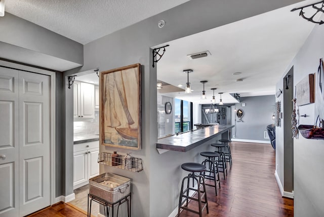 kitchen with a textured ceiling, dark hardwood / wood-style floors, white cabinetry, backsplash, and a breakfast bar area