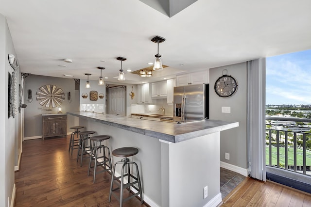 kitchen featuring pendant lighting, sink, stainless steel refrigerator with ice dispenser, white cabinets, and a kitchen bar