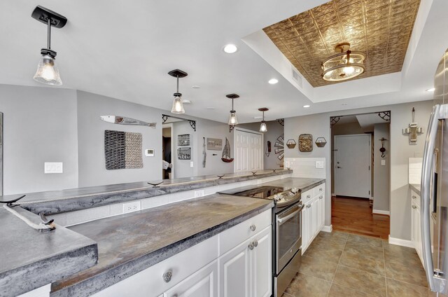 kitchen featuring light tile patterned floors, white cabinetry, stainless steel electric stove, a raised ceiling, and decorative light fixtures