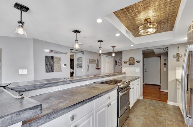 kitchen featuring a raised ceiling, appliances with stainless steel finishes, pendant lighting, and white cabinets