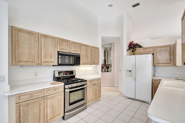 kitchen with light tile patterned flooring, sink, white fridge with ice dispenser, light brown cabinetry, and gas stove