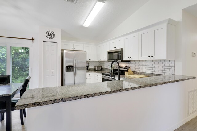 kitchen featuring appliances with stainless steel finishes, decorative backsplash, kitchen peninsula, and lofted ceiling