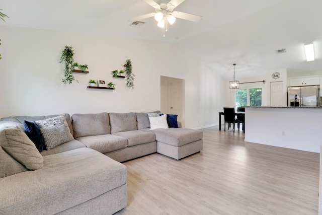 living room featuring light hardwood / wood-style flooring, ceiling fan with notable chandelier, and vaulted ceiling