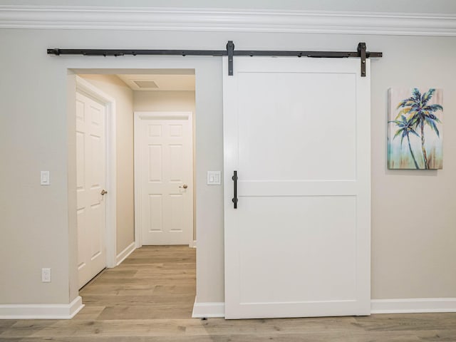 hall with light wood-type flooring, a barn door, and crown molding