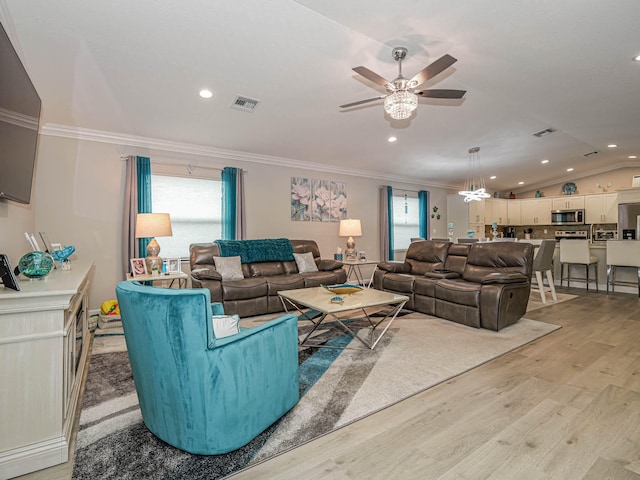 living room featuring ornamental molding, ceiling fan with notable chandelier, vaulted ceiling, and light hardwood / wood-style floors