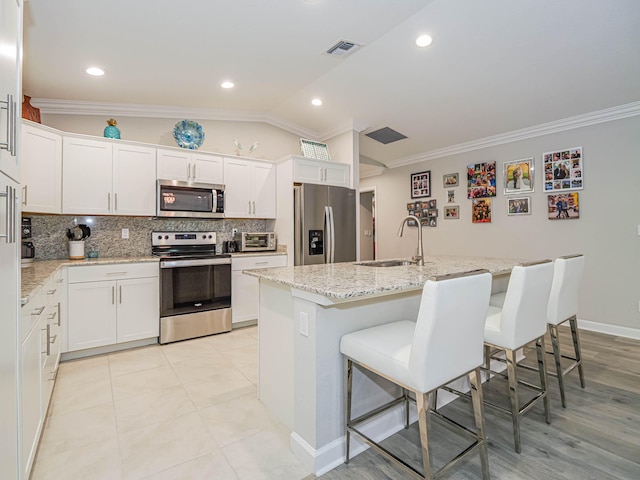 kitchen featuring tasteful backsplash, stainless steel appliances, a kitchen island with sink, white cabinets, and sink