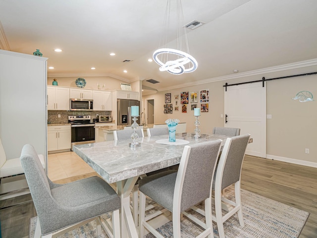 dining space with lofted ceiling, a barn door, ornamental molding, light hardwood / wood-style floors, and a chandelier